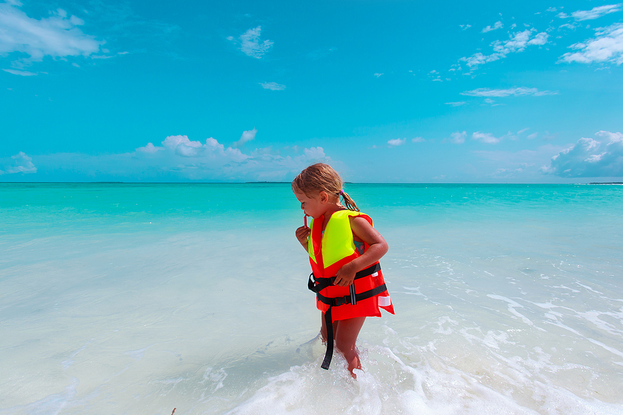 small girl wearing life jacket at the edge of the water at the beach demonstrating beach safety