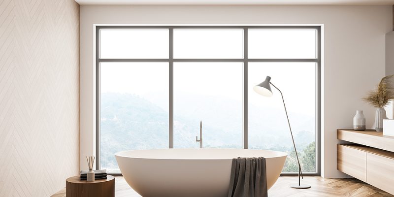 minimalist high end bathroom with white tub, gray bath towel, large windows and foggy mountain view