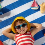 Happy small boy lying on blue and white striped cotton beach towel with beach toys around him