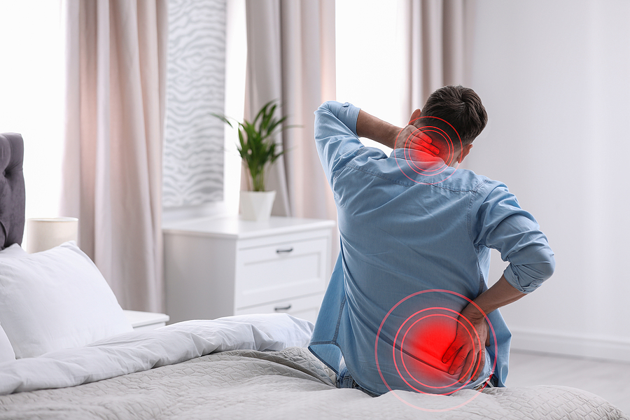 Man suffering from back and neck pain after sleeping on uncomfortable pillow or mattress at home