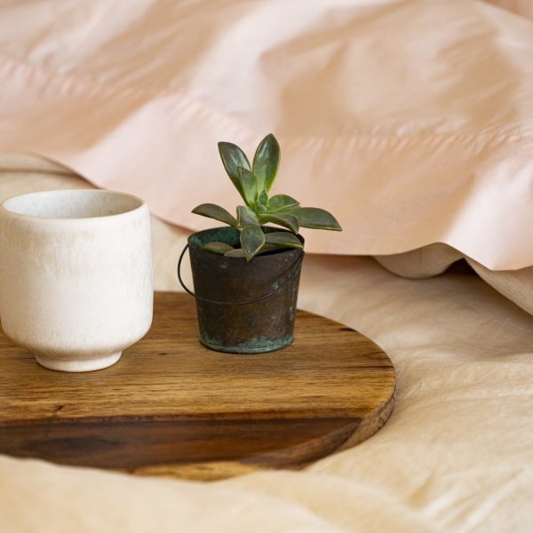 close up of soft bed with linen duvet cover and pink bedding with mug of hot coffee and a small plant on a wooden tray