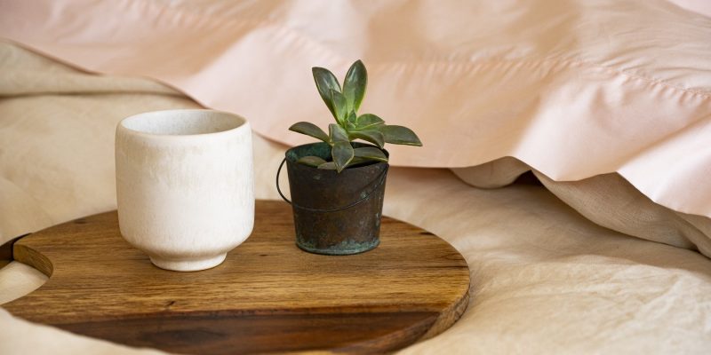 close up of soft bed with linen duvet cover and pink bedding with mug of hot coffee and a small plant on a wooden tray