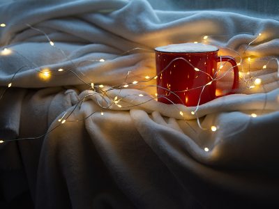 Holiday image of red and white mug of coffee or cocoa on white plaid with christmas lights.