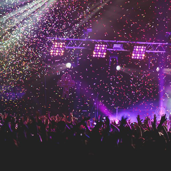A crowded concert hall with scene stage lights, rock show performance, with people silhouette, colorful confetti explosion fired on dance floor during a concert festival