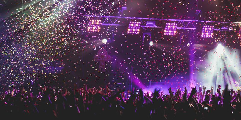 A crowded concert hall with scene stage lights, rock show performance, with people silhouette, colorful confetti explosion fired on dance floor during a concert festival