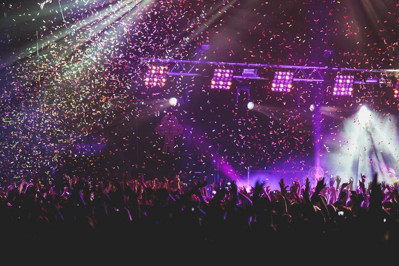 A crowded concert hall with scene stage lights, rock show performance, with people silhouette, colorful confetti explosion fired on dance floor during a concert festival