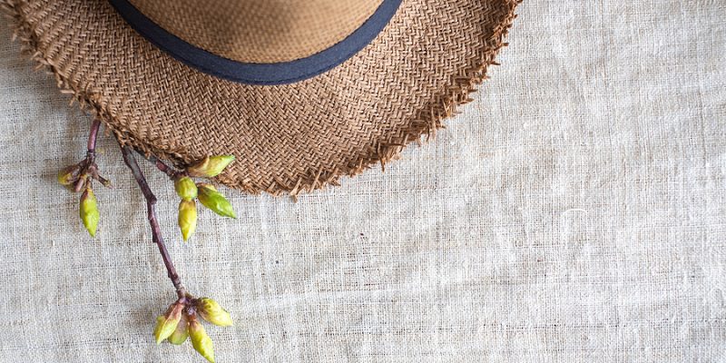 Top view of Summer brown panama straw hat with flower plant on organic linen