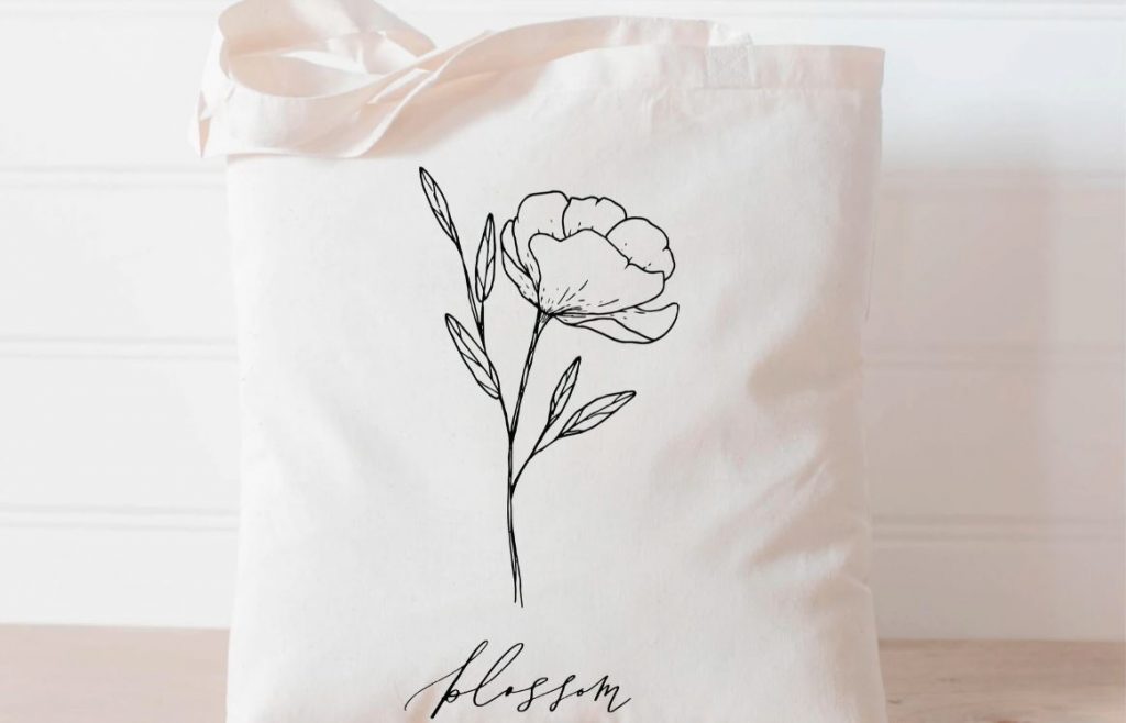 white organic linen tote bag with wildflower pattern and blossom lettering etching