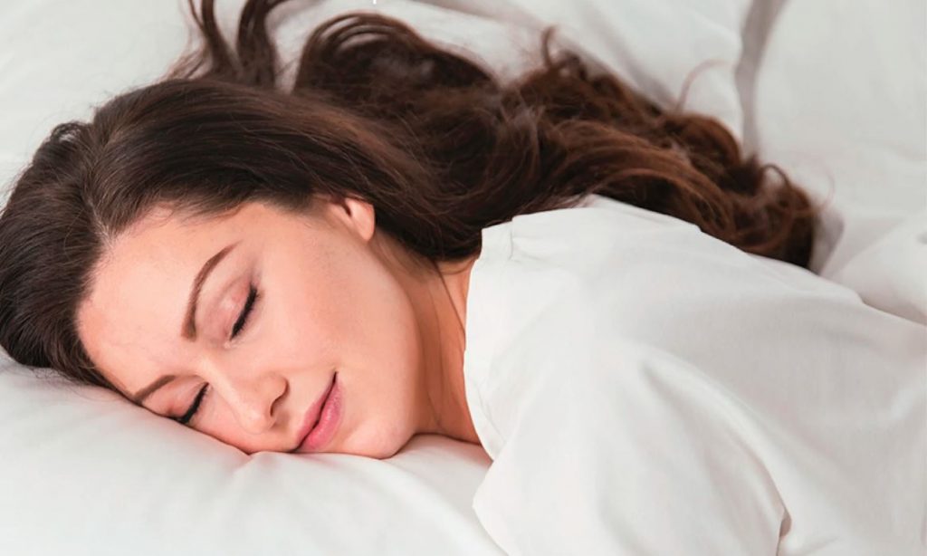 woman smiling as she sleeps comfortably on her stomach on a soft pillow with good neck alignment