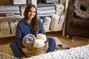Happy woman holding basket of linens in front of organized linen shelves