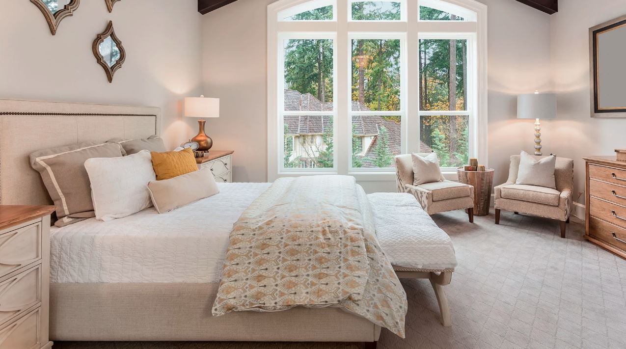 Luxury bedding in an expansive bedroom space against a muted pink background and large vaulted windows.