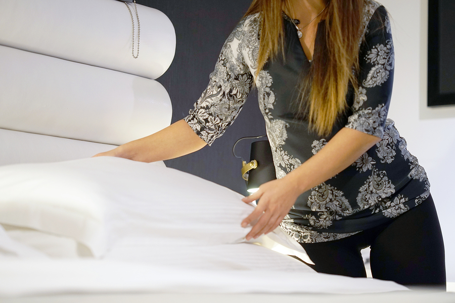 Woman with hotel linens, placing hotel pillows on bed