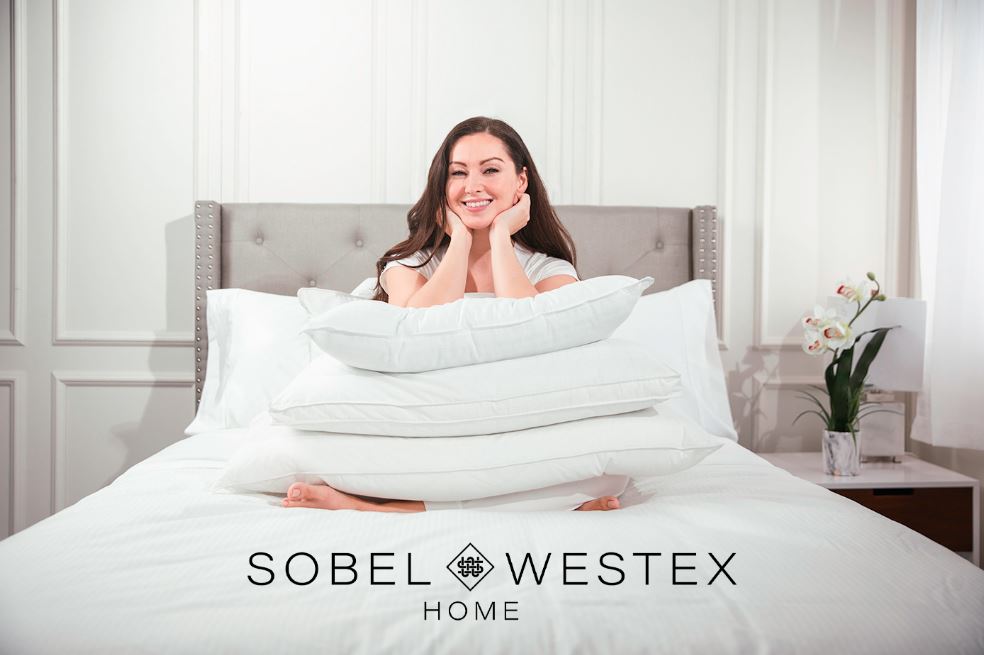 Woman sitting on bed with stacked pillows on her lap, featuring logo for Luxury Hotel Linen Brand Sobel Westex