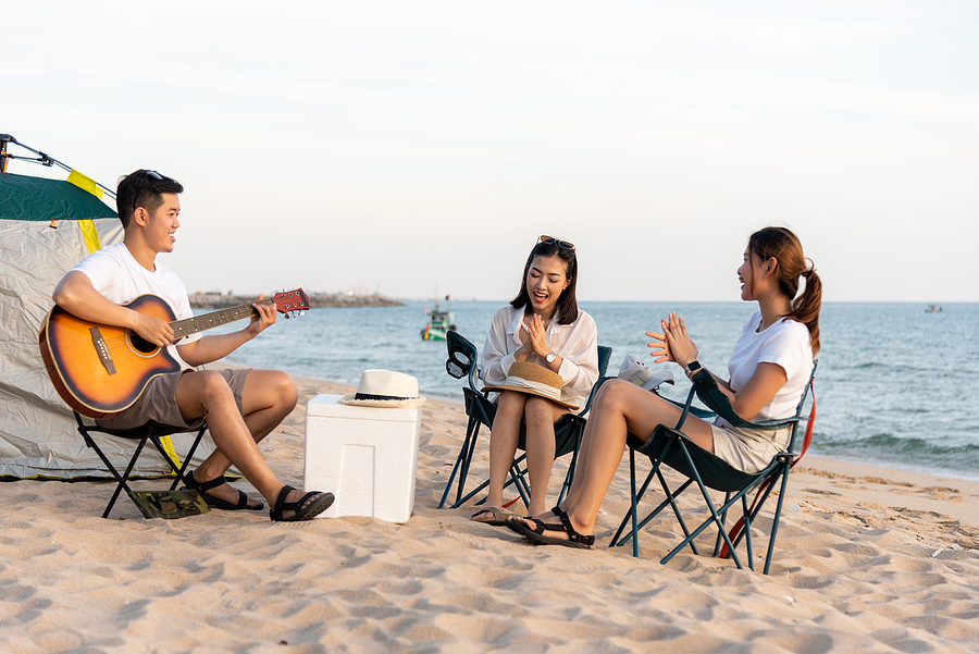 Beach fun with friends, guitar playing on chairs with resort essentials like cooler and hat.