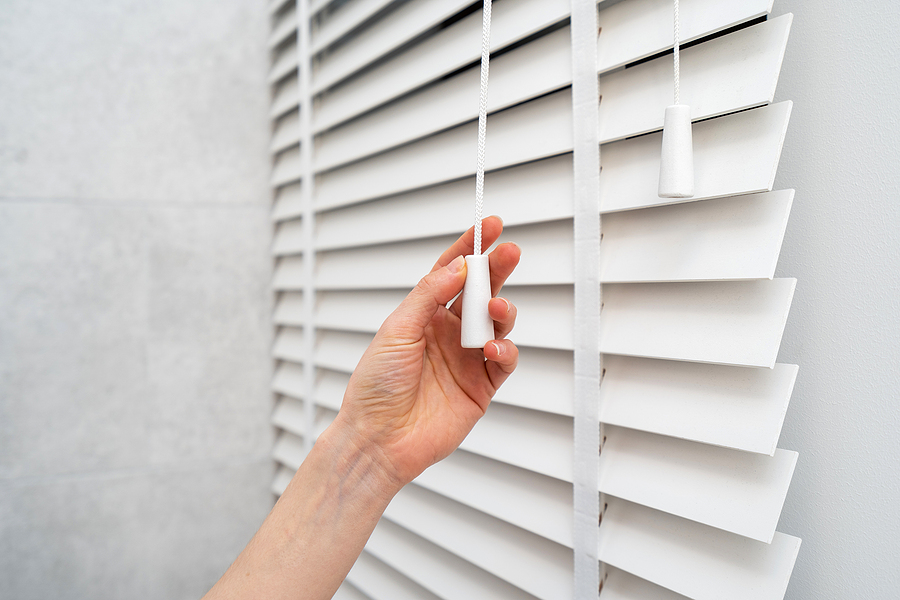 woman adjusting blinds to keep the house cool in warm summer months